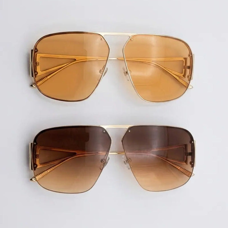 Pair of gold-framed sunglasses with brown lenses on a light gray background