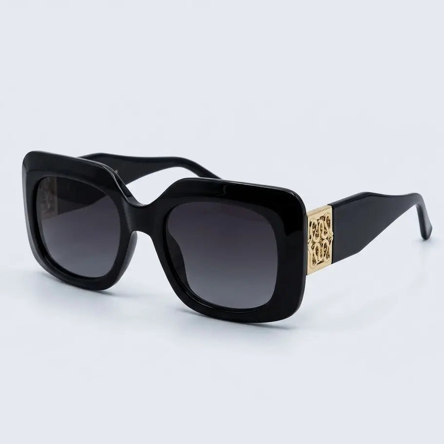 Black square sunglasses with dark lenses and a gold-tone decorative accent on the temple arm, shown on a light gray background.