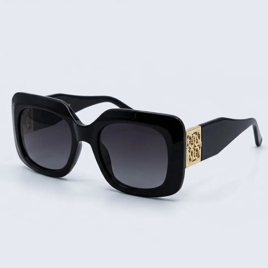 Black square sunglasses with dark lenses and a gold-tone decorative accent on the temple arm, shown on a light gray background.