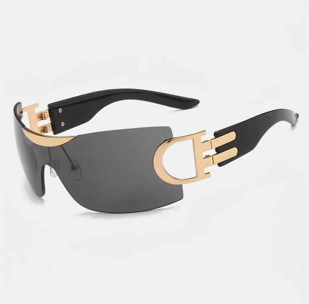 Rimless shield-style sunglasses with dark gray lenses, gold side accents, and black arms displayed on a light gray background.