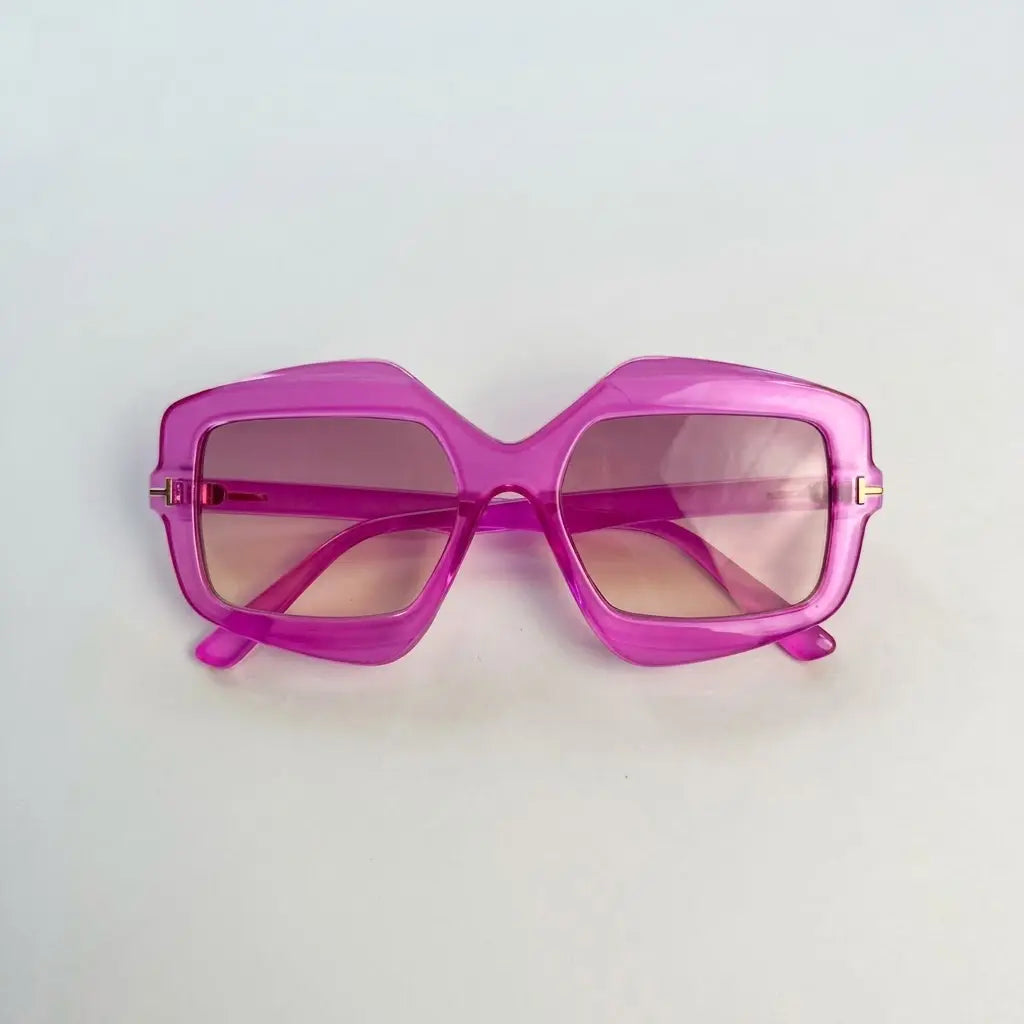 A pair of oversized square sunglasses with a translucent bright pink frame and pink-tinted lenses, photographed on a plain light background.