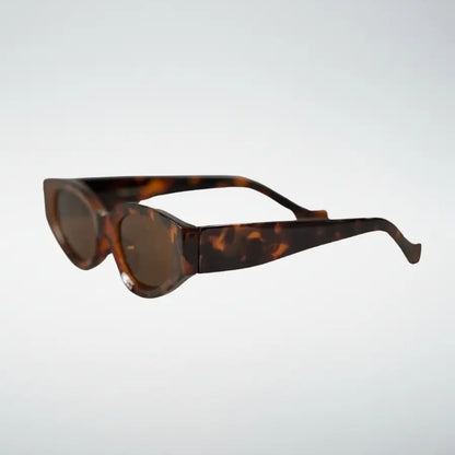 Tortoiseshell cat-eye sunglasses with dark brown lenses, shown floating against a light gray gradient background.