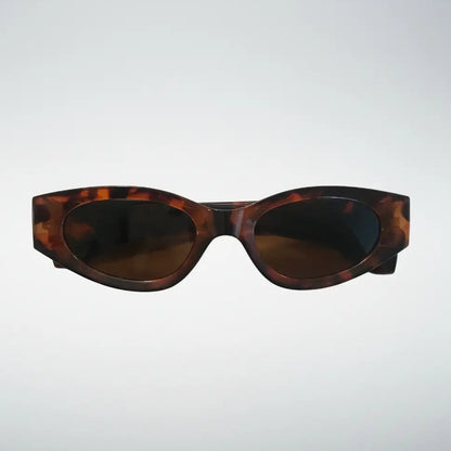 Oval sunglasses with a dark brown and amber tortoiseshell acetate frame and dark tinted lenses, shown against a light gray gradient background.