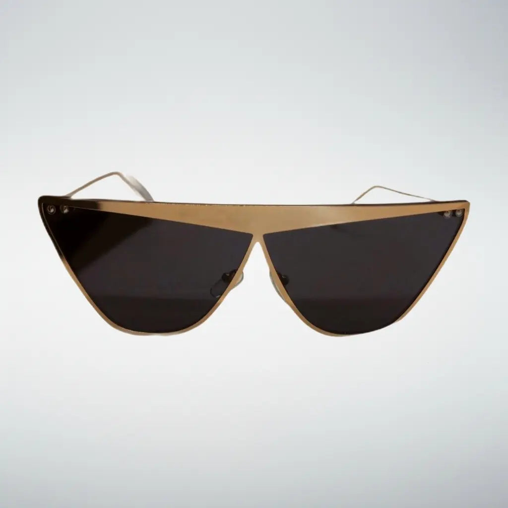 Triangular shield sunglasses with a gold metal frame and dark tinted lenses, shown against a light gray gradient background.