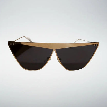 Triangular shield sunglasses with a gold metal frame and dark tinted lenses, shown against a light gray gradient background.
