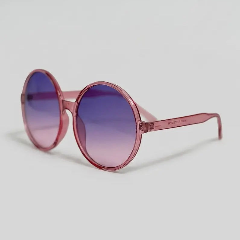 Side view round sunglasses with a translucent pink frame and purple-to-pink gradient lenses displayed on a light gray background.