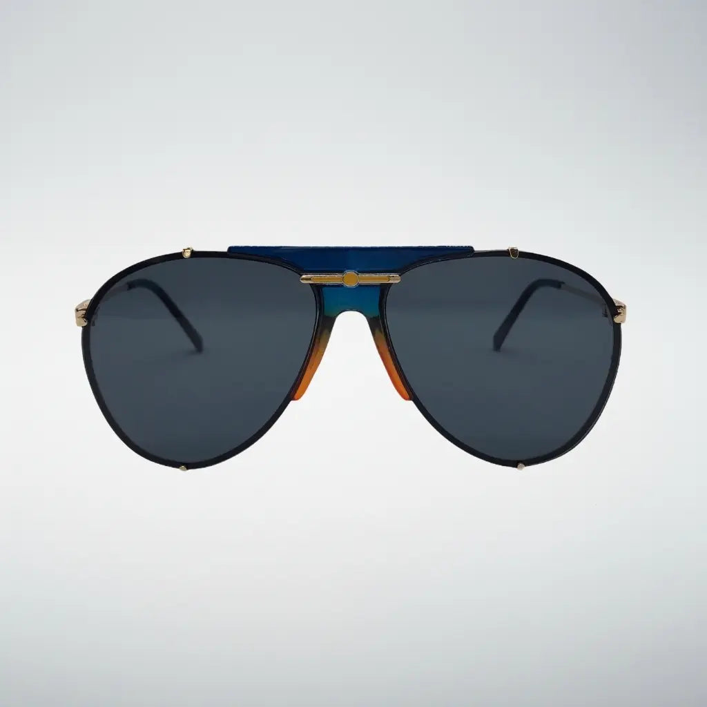 Aviator sunglasses with dark blue lenses, a black frame, gold metal accents, and a distinctive blue and orange gradient bridge, shown against a light gray background.