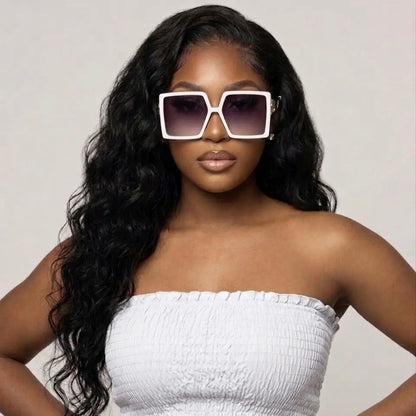 Woman wearing a white strapless top and large sunglasses against a plain background