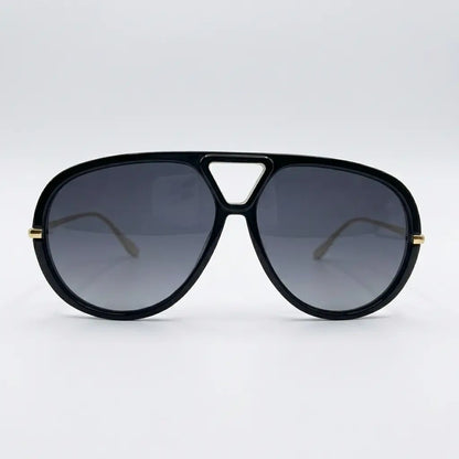 Oversized aviator-style sunglasses with a black frame, black lenses, and thin gold metal arms displayed on a light gray background.