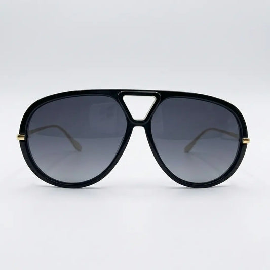 Oversized aviator-style sunglasses with a black frame, black lenses, and thin gold metal arms displayed on a light gray background.