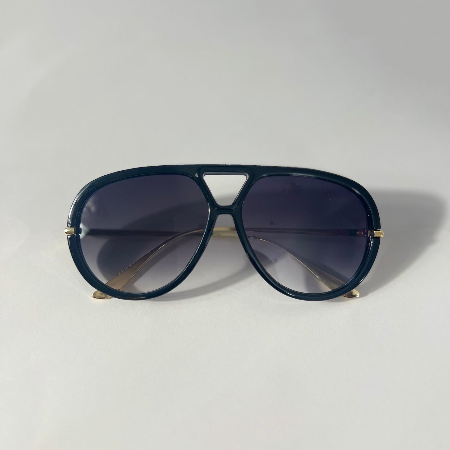 Black sunglasses with slight purple gradient lens with a gold frame on a light gray background