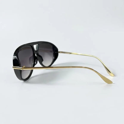 Side profile view of oversized aviator-style sunglasses with a black frame, black lenses, and thin gold metal arms displayed on a light gray background.